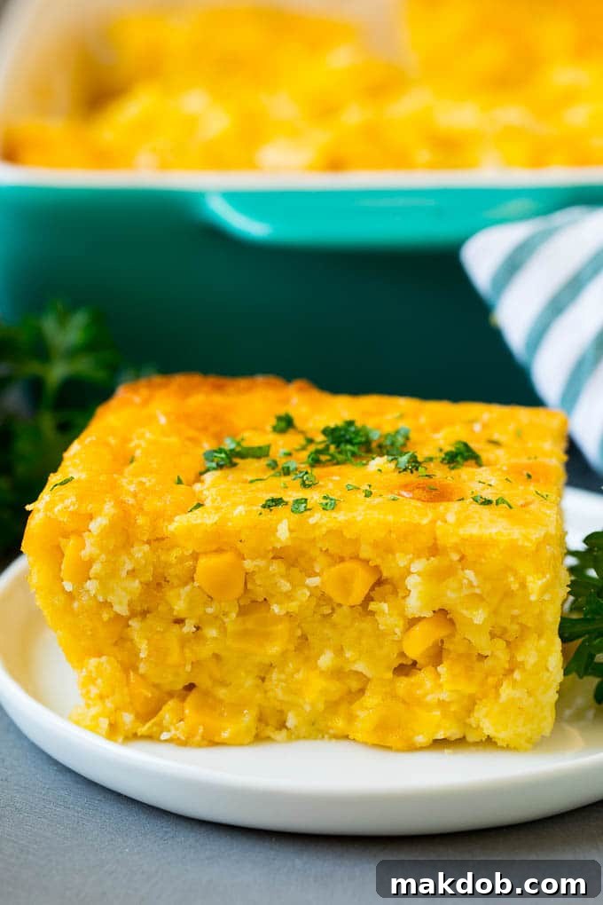 This corn souffle recipe is a flavorful blend of corn kernels, butter, eggs and creamed corn, all baked to light and fluffy perfection. A perfectly portioned slice of corn souffle on a white plate, ready to be enjoyed.