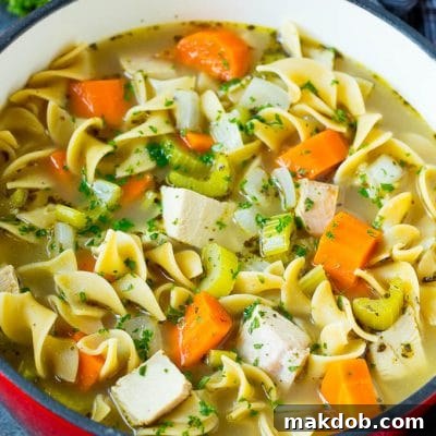 Turkey soup with egg noodles and colorful vegetables in a pot.
