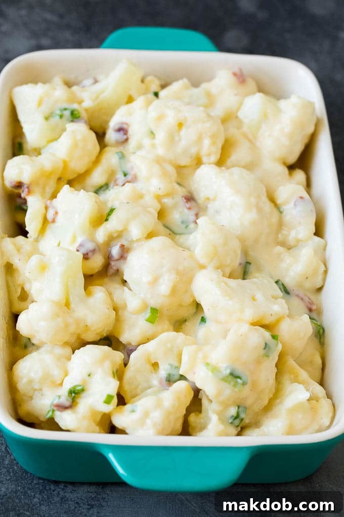 Creamy cauliflower mixture, perfectly prepped for baking. Cauliflower florets generously coated in a creamy cheese sauce, mixed with bacon and green onions, in a baking dish.