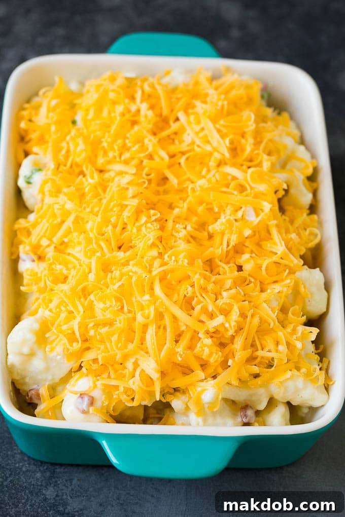 Unbaked cauliflower casserole, topped with cheddar cheese, awaiting its golden finish. Cauliflower casserole in a baking dish, topped with a generous layer of shredded cheese, ready for the oven.