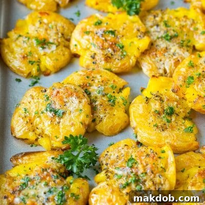 Crispy smashed potatoes on a sheet pan, generously topped with glistening garlic butter and fresh green parsley, ready to be served.