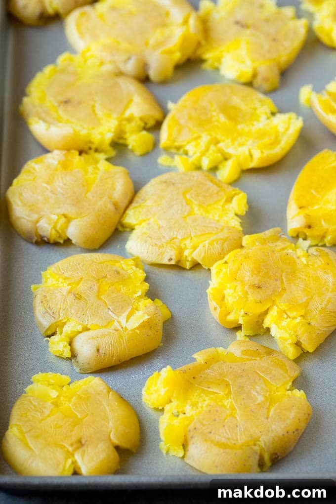 Perfectly flattened baby potatoes arranged neatly in a single layer on a sheet pan, ready for butter and seasoning.