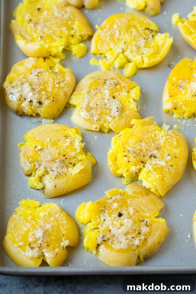 Crispy smashed potatoes topped with melted garlic butter, fresh herbs, and a golden layer of grated cheese on a baking sheet.