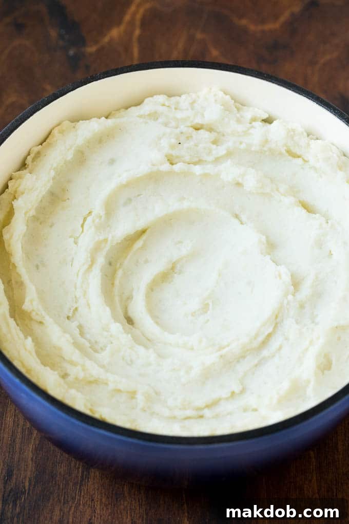Cream Cheese Mashed Potatoes in a Blue Pot Creamy cream cheese mashed potatoes in a rustic blue pot, garnished with a pat of butter and fresh chives, ready to be served.