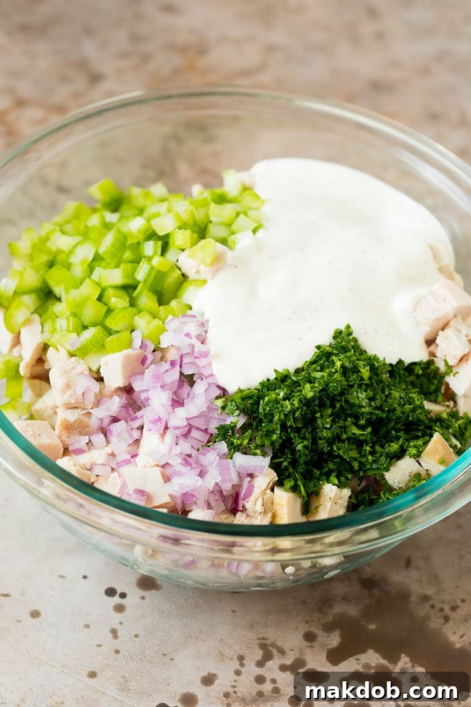This turkey salad is a blend of diced turkey and colorful veggies, all tossed in a savory creamy dressing. A bowl of turkey and vegetables with a creamy dressing poured over the top, ready to be mixed.