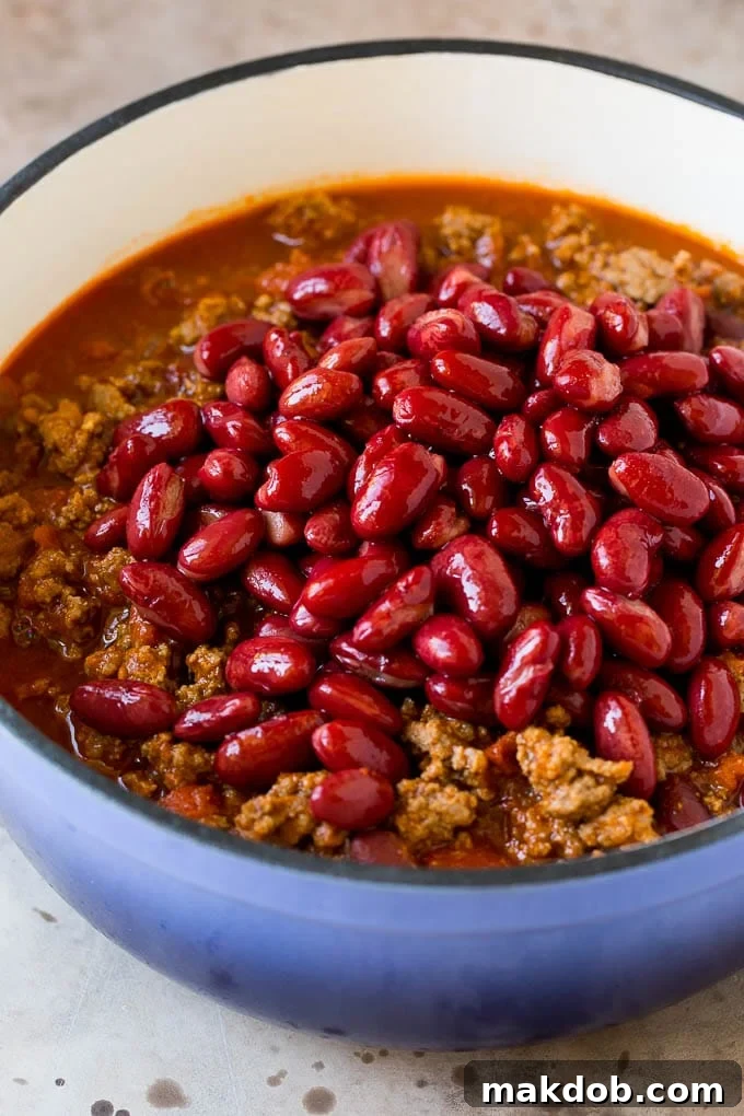 This beef chili is a blend of meat, tomatoes, spices and beans, all simmered together to make a delicious and hearty meal. Kidney beans in a blue pot with a ground beef and tomato mixture.