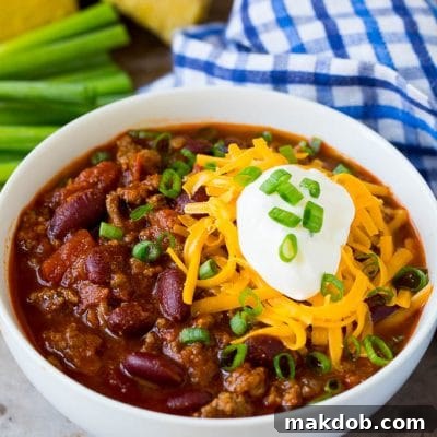 A bowl of beef chili topped with cheese, sour cream and green onions.