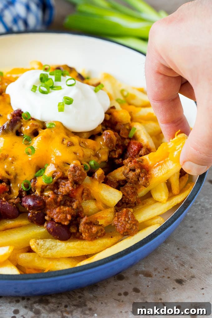 A hand reaching for chili cheese fries.