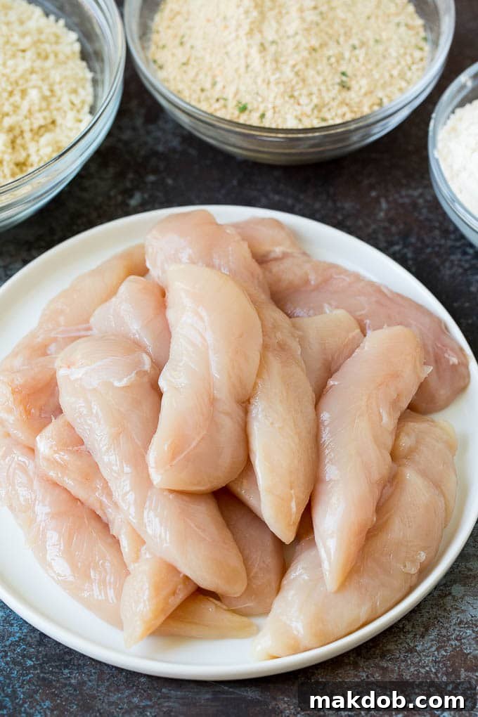 Bowls of raw chicken tenders, seasoned flour, whisked eggs, and a breadcrumb mixture, ready for coating.