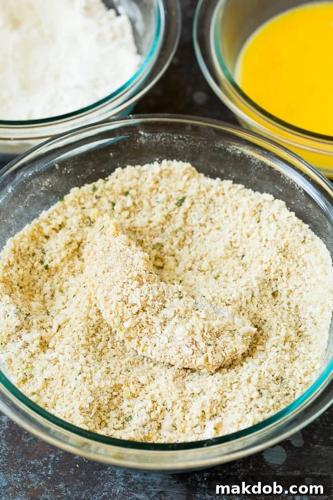 A piece of chicken being coated in a bowl of parmesan breadcrumbs.