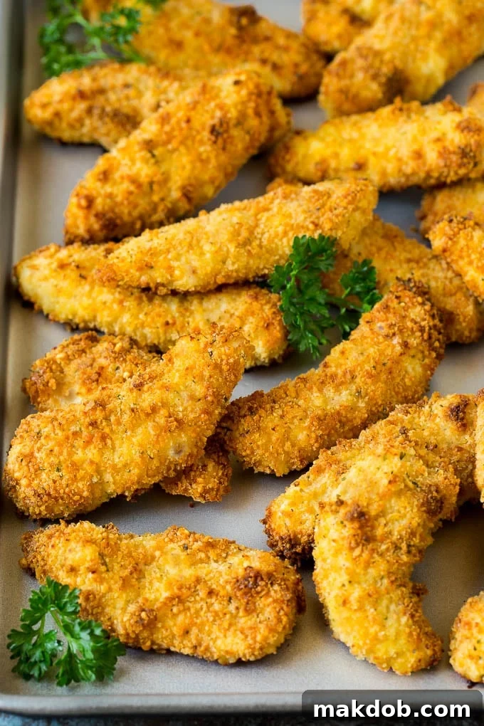 Oven-baked chicken tenders arranged on a sheet pan and garnished with fresh parsley.