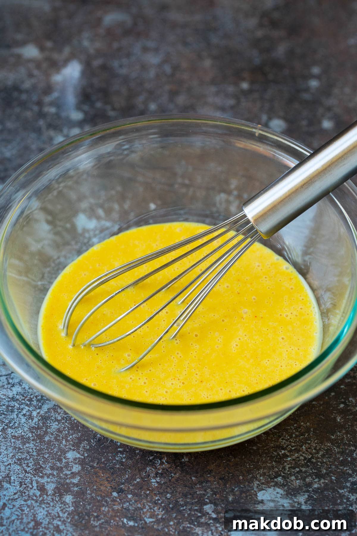A whisk in a bowl of honey mustard.