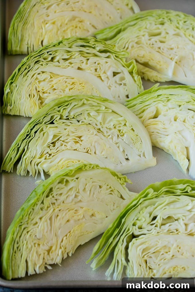 This roasted cabbage recipe is wedges of cabbage seasoned with olive oil and spices, then oven baked until tender and browned. Raw green cabbage wedges arranged on a baking sheet, ready for seasoning.