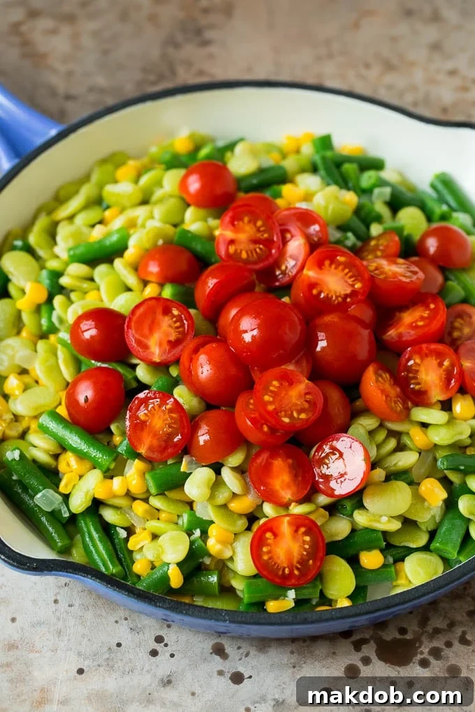 A pile of cherry tomatoes on top of a mixture of corn and beans.