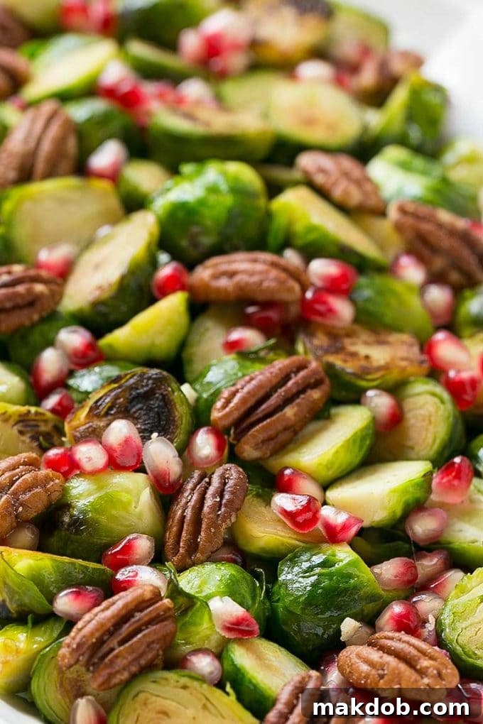 Close-up of roasted Brussels sprouts adorned with bright red pomegranate seeds and golden halved pecans.