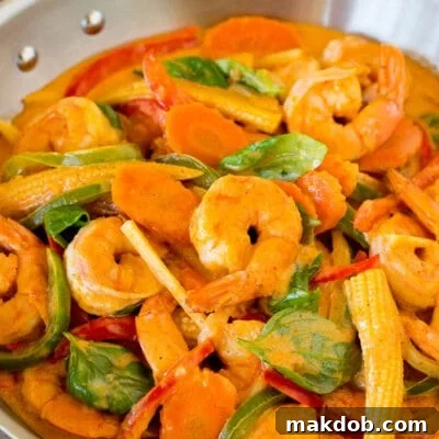 A pan of shrimp curry with assorted vegetables and fresh basil.