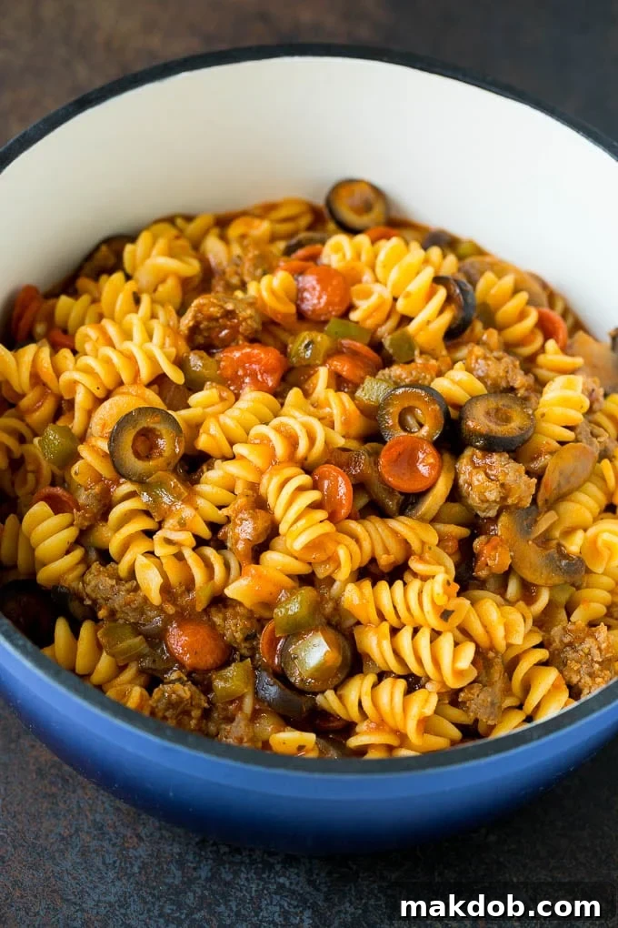 Cooked pasta with meat and vegetables combined in a pot, ready for baking. Cooked pasta, Italian sausage, sautéed vegetables, and rich tomato sauce thoroughly mixed together in a large pot, perfectly combined and ready to be transferred to a baking dish for the final bake.