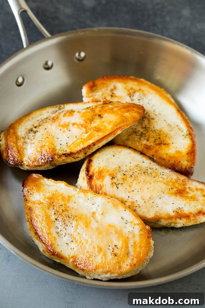 Close-up of golden brown chicken breasts searing in a pan with olive oil.