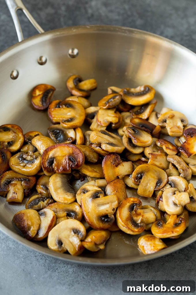 Close-up of sliced mushrooms being sautéed in a skillet with butter.
