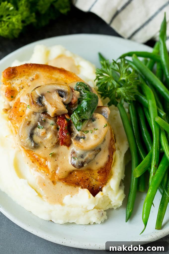 Tuscan chicken served on a plate with creamy mashed potatoes and vibrant green beans.
