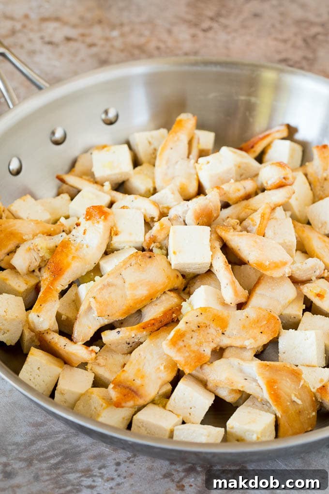Chicken and tofu being sautéed together in a hot pan, browning perfectly for a Pad Thai dish.