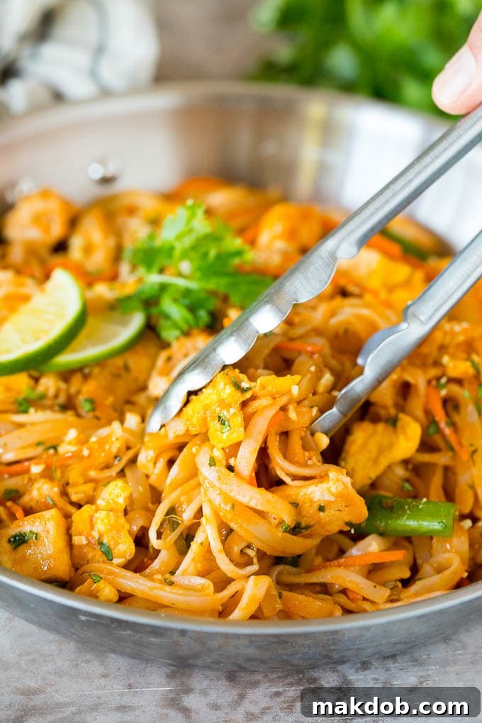 Tongs gracefully serving a portion of Chicken Pad Thai from a pan onto a plate, highlighting the stir-fried noodles and ingredients.