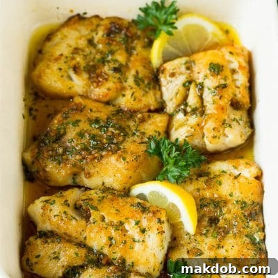 A pan of baked cod garnished with lemon and parsley.