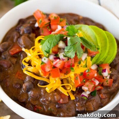 A bowl of black bean soup topped with salsa, avocado and cheese.