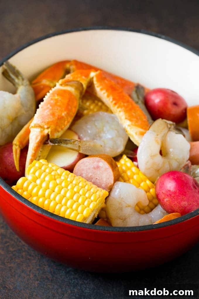 This Low Country Boil is a blend of shrimp, crab, sausage, corn and potatoes, all cooked together to create a hearty dinner. Assorted seafood, sausage and corn in a red pot.