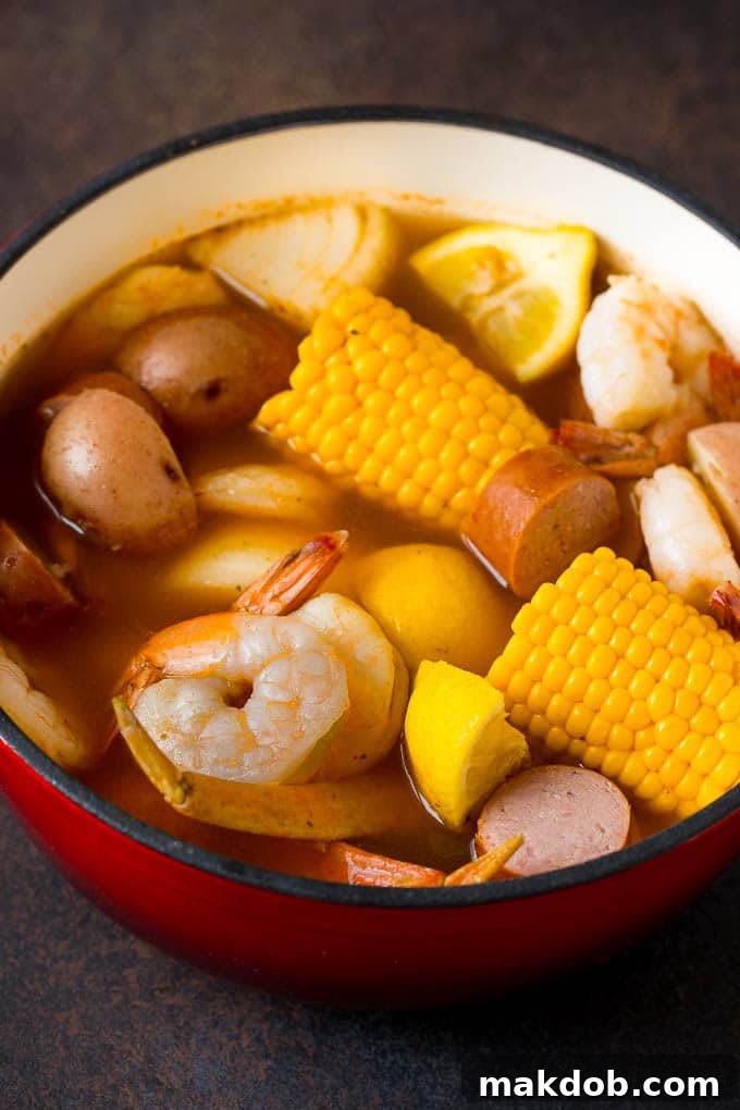 This Low Country Boil is a blend of shrimp, crab, sausage, corn and potatoes, all cooked together to create a hearty dinner. Boiled shrimp, potatoes and corn in a red pot.