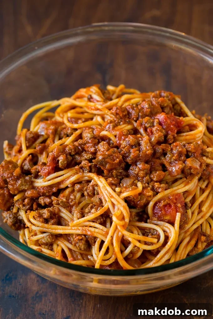 Spaghetti tossed with meat sauce Cooked spaghetti tossed with the rich, savory meat sauce in a large mixing bowl, ensuring every strand is coated for maximum flavor.
