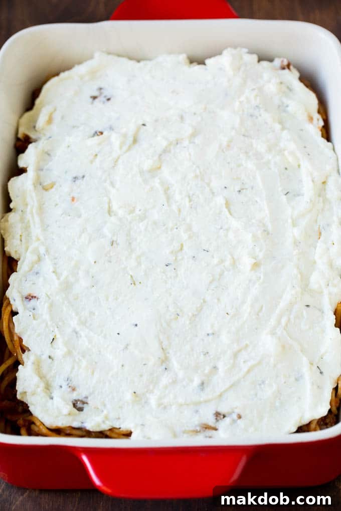 Ricotta cheese spread over spaghetti A creamy layer of ricotta and cream cheese spread smoothly over a bed of spaghetti and meat sauce in a baking dish, forming the 'million dollar' center.