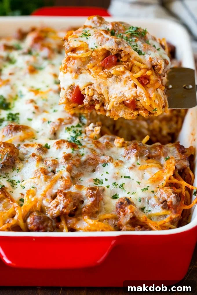 Serving Million Dollar Spaghetti A spatula serving a generous portion of Million Dollar Spaghetti Casserole from a baking dish, showcasing its cheesy, layered goodness.