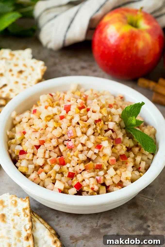 This charoset recipe is a blend of apples, walnuts and honey, all mixed together to make a sweet spread that's an essential part of any Passover meal. A beautifully presented bowl of charoset, garnished with fresh mint, served alongside matzo crackers.