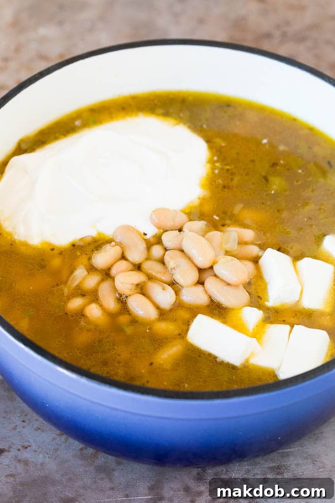 This white chicken chili is a creamy blend of chicken, chilies, beans and spices, all simmered together A pot of broth and chicken with beans, sour cream and cream cheese.