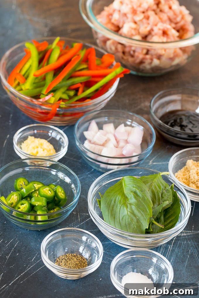 Prepped ingredients for Thai basil chicken recipe, including diced chicken, sliced bell peppers, fresh basil leaves, and serrano chilies.
