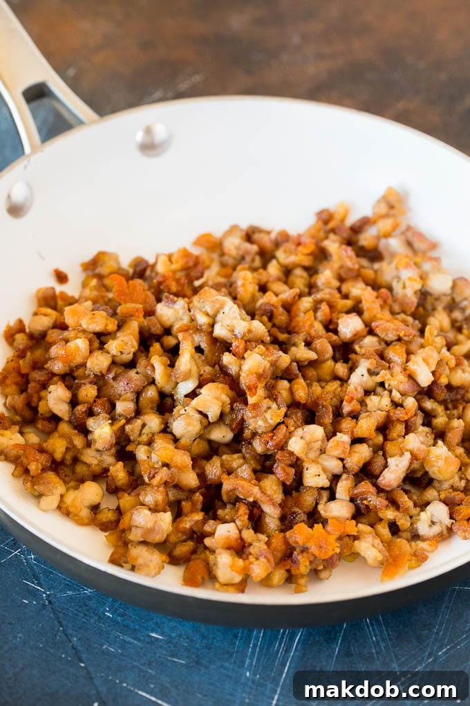 Close-up of browned, diced chicken thighs cooking in a hot skillet, seasoned with salt and pepper.