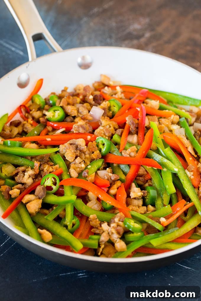 Chicken, bell peppers, serrano chilies, and minced garlic being stir-fried together in a pan, emitting aromatic steam.