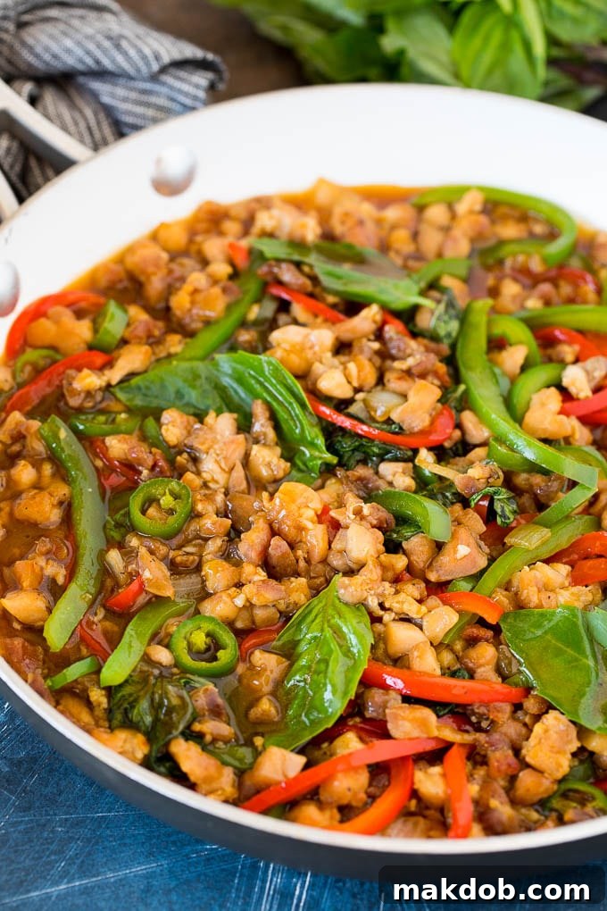 A pan filled with freshly cooked Thai Basil Chicken stir-fry, featuring glistening chicken, colorful peppers, and vibrant fresh basil leaves, ready to be served.