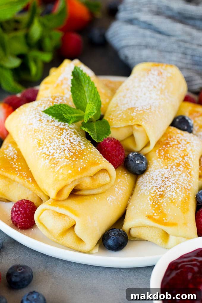 Cheese blintzes garnished with powdered sugar and berries on a plate.