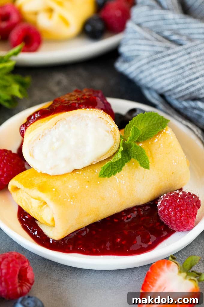 A plate of cheese blintzes with raspberry sauce and fresh fruit for serving.
