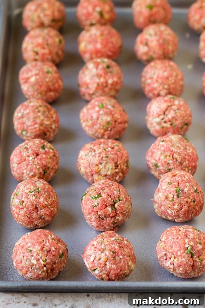 Meatballs lined up on a sheet pan, ready for broiling.