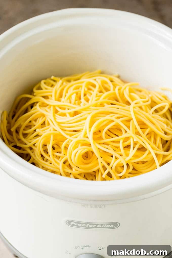 Cooked pasta inside a slow cooker with meatballs and sauce.