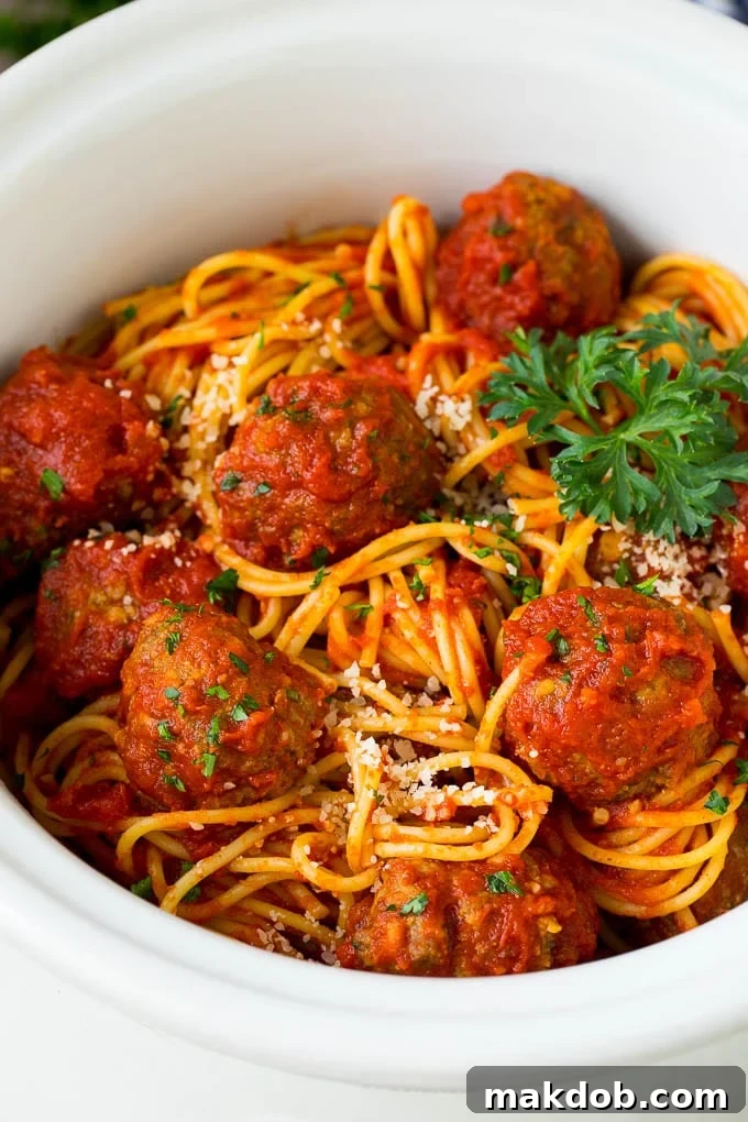 Crock pot spaghetti with meatballs, parmesan and fresh parsley in a bowl.