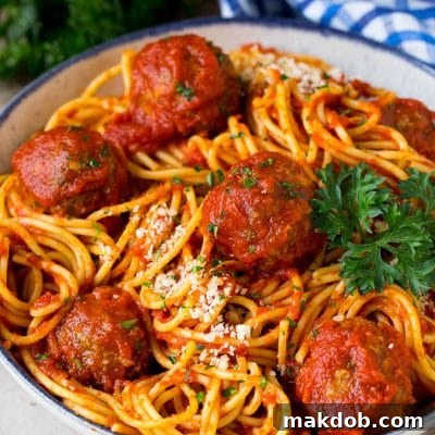 A serving bowl of crock pot spaghetti topped with meatballs and grated cheese.