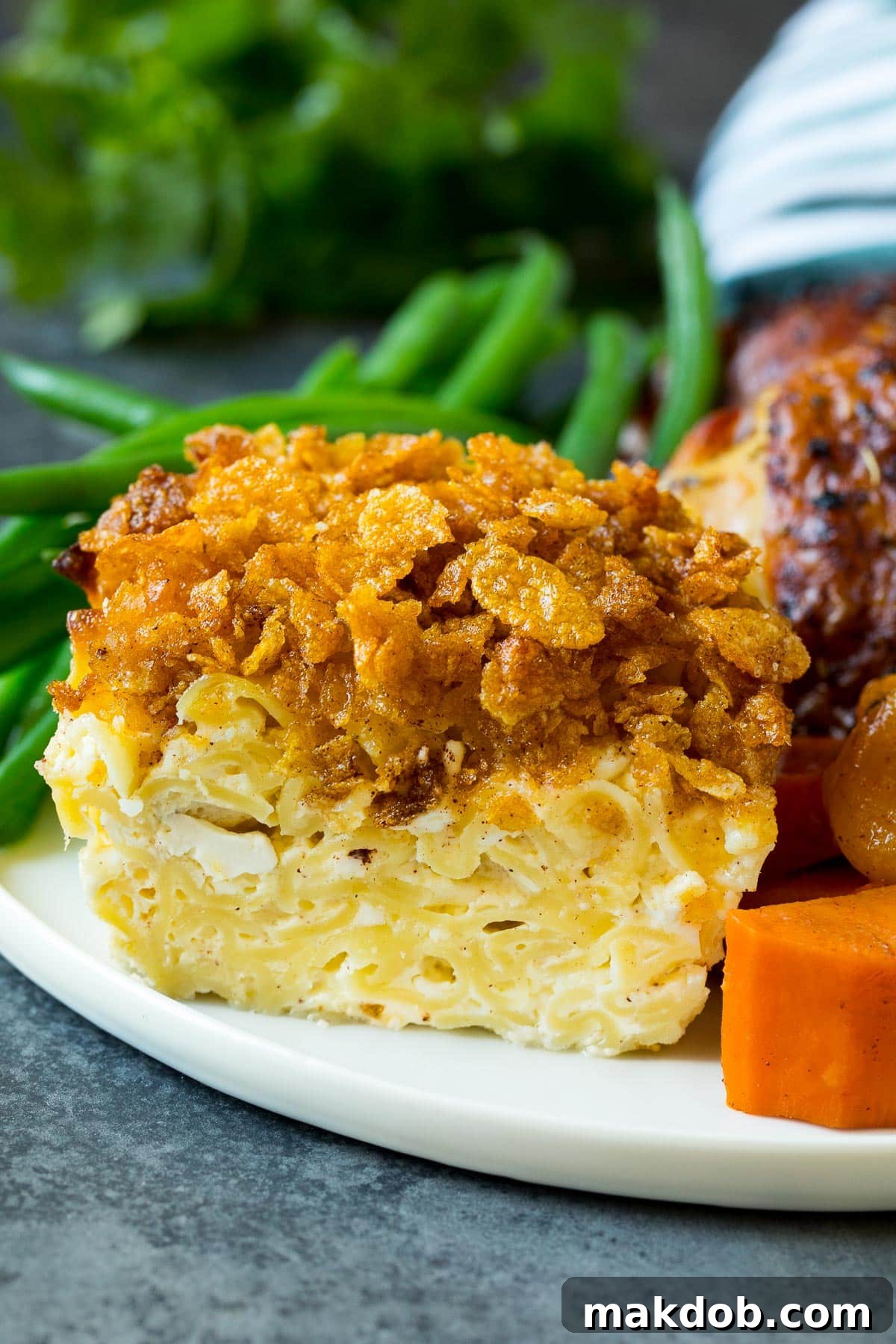 Golden Noodle Delight 2 A generous portion of golden-baked noodle kugel served alongside roasted chicken and fresh green vegetables on a white plate.