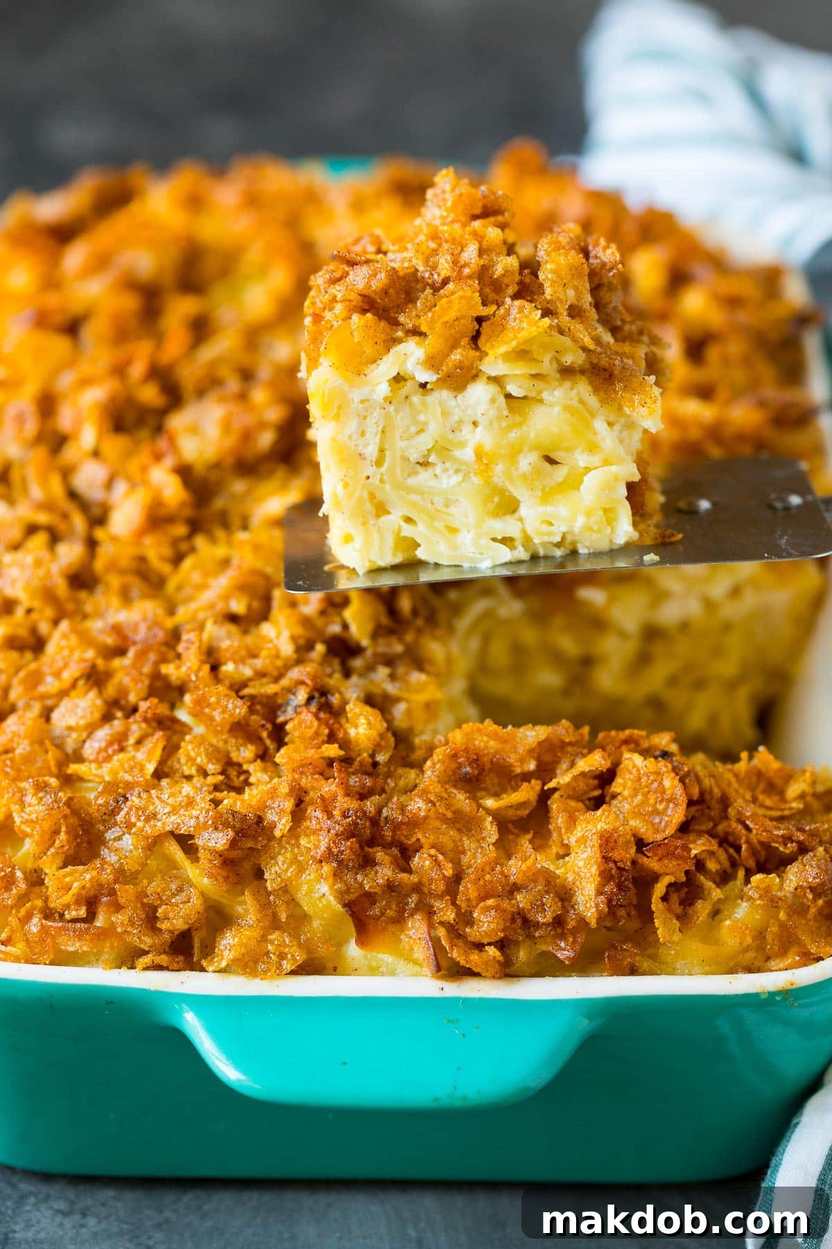 Golden Noodle Delight 7 A serving spatula lifting a square portion of noodle kugel from the baking dish, showcasing its golden-brown topping and soft interior.