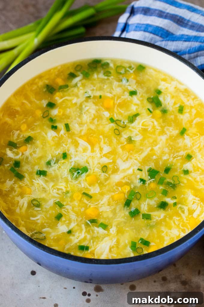 A pot of egg drop soup with corn and sliced green onions.