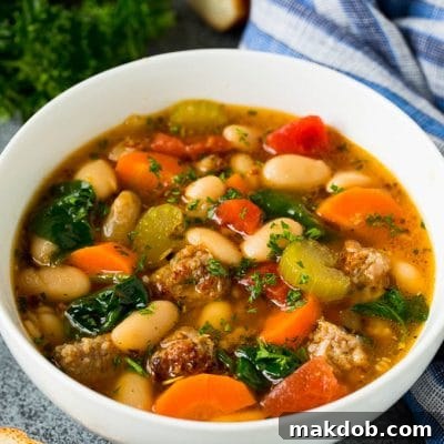 A bowl of white bean soup with Italian sausage, tomatoes and spinach.