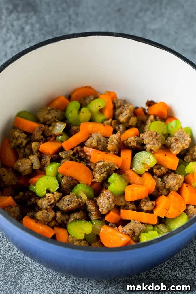 Sausage and Vegetables Sautéing for Soup Sizzling Italian sausage, finely diced carrots, and celery cooking in a large soup pot, releasing an irresistible aroma as they form the base for the Tuscan White Bean Soup.